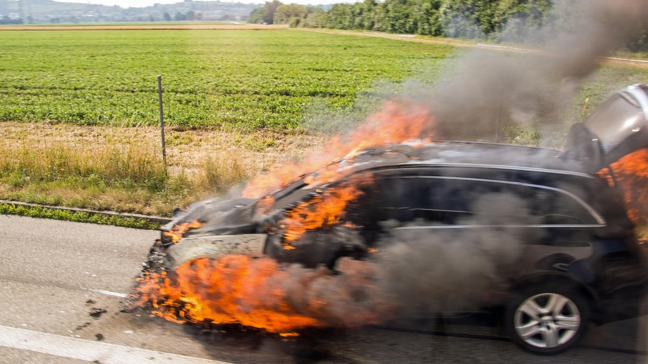 Brennendes Fahrzeug am Strassenrand vor einem Feld.