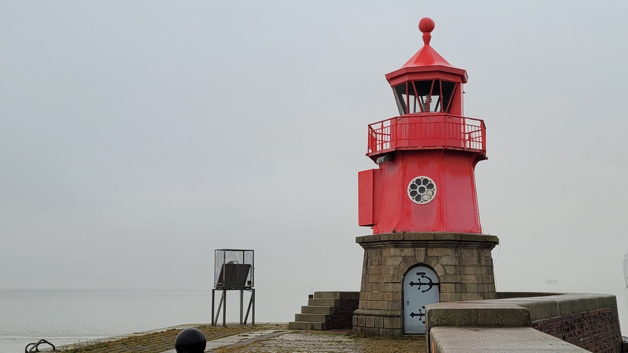 Ein kleiner roter Leuchtturm nah am Wasser