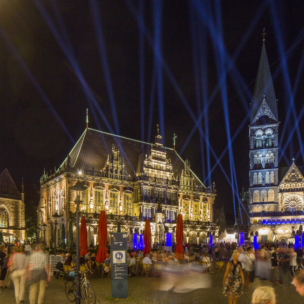 Viele Leute auf Bremens blau illuminiertem Marktplatz im Dunkeln