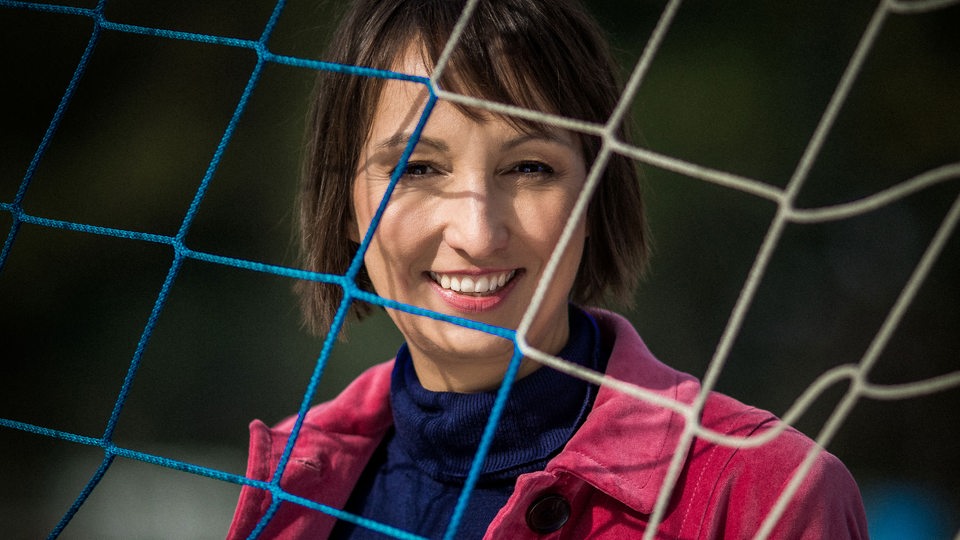 Eine Frau mit roter Jacke steht hinter einem Tornetz.