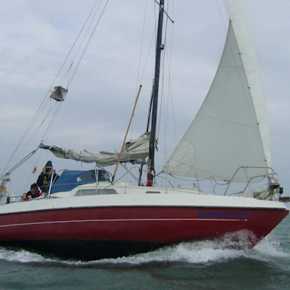 Ein rotes Segelboot mit Seglern fährt auf offenem Meer.