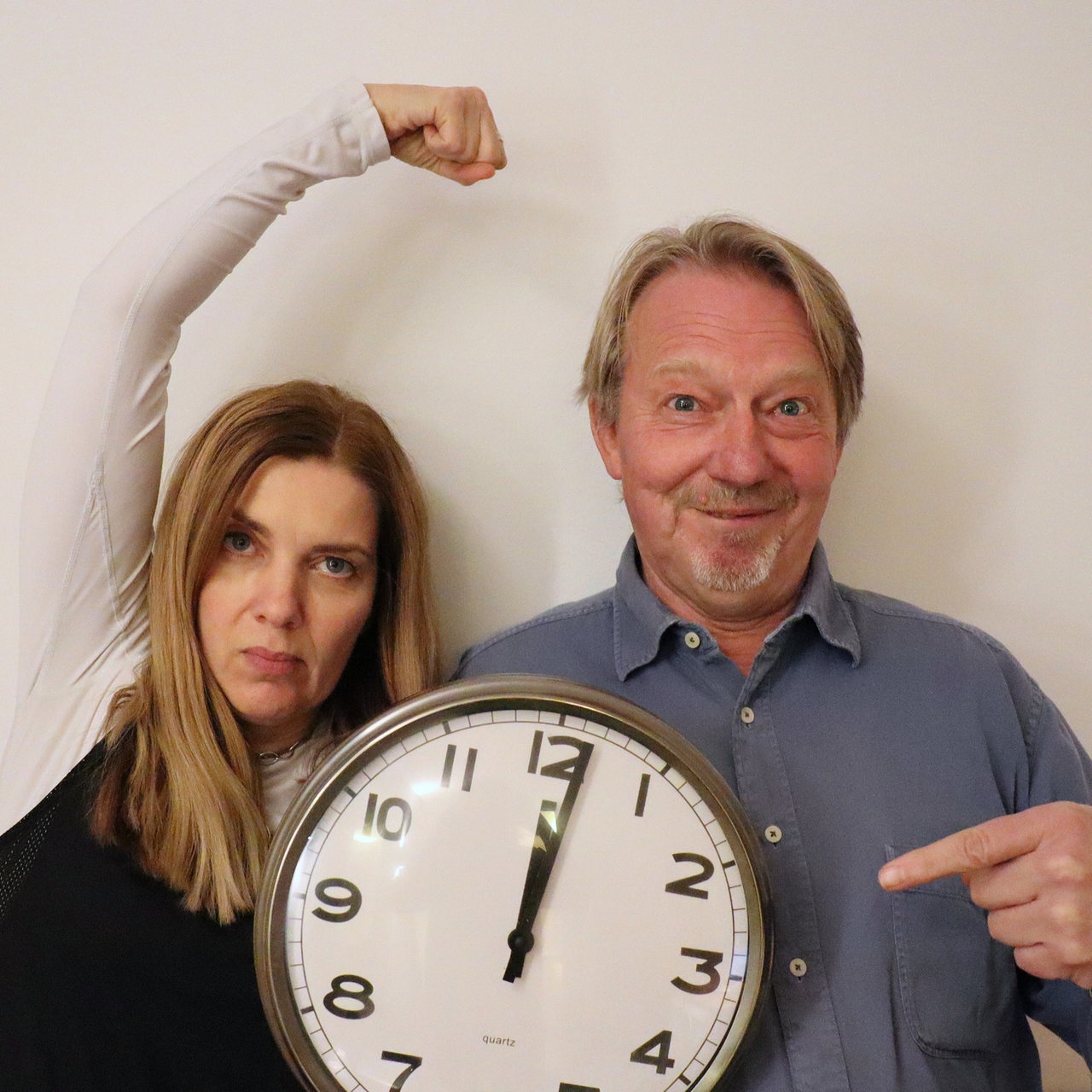 Tina Voß und Dietmar Wischmeyer halten eine Uhr, die auf kurz nach 12 steht.